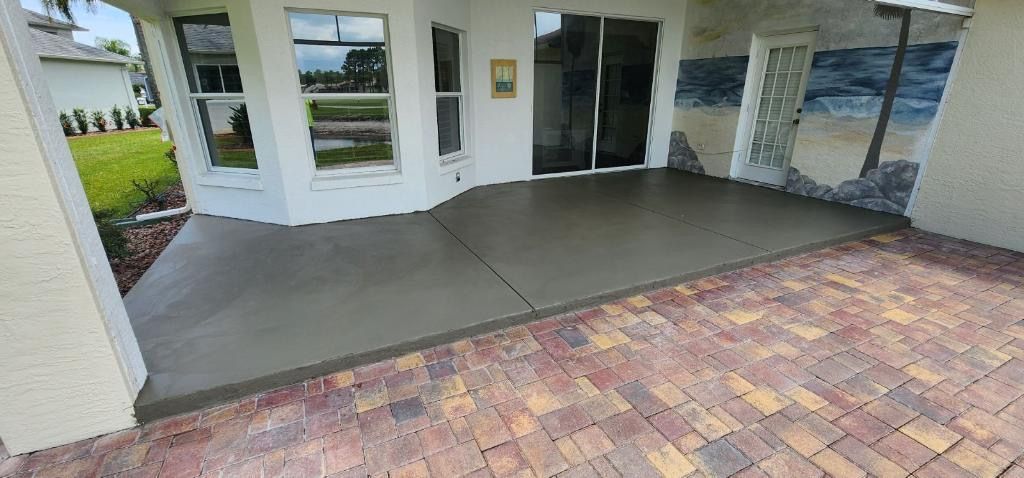 A patio with a new concrete section, bordered by brick pavers. House exterior visible. A patio with a new concrete section, bordered by brick pavers. House exterior visible.