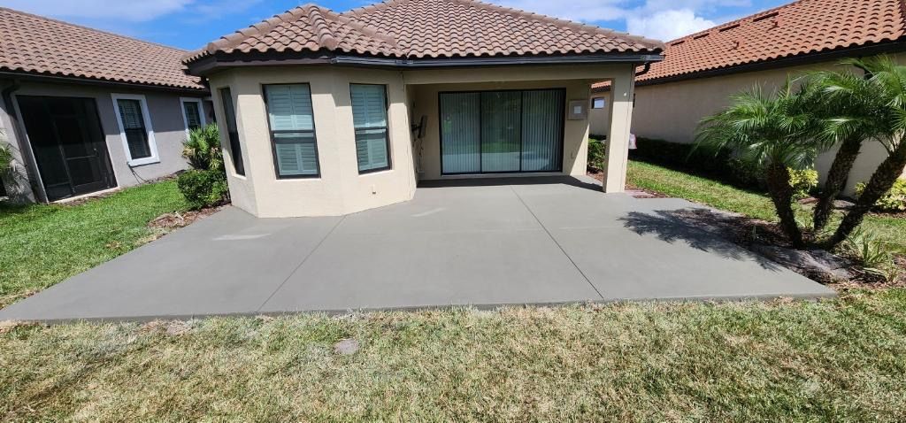 A beige house with a concrete patio and a grassy yard under a blue sky.