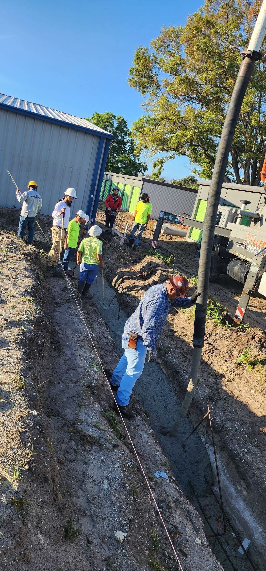 Construction workers filling a trench with concrete. Gray dirt, blue sky, and a few trees. Construction workers filling a trench with concrete. Gray dirt, blue sky, and a few trees.