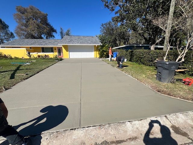 New concrete driveway in front of a yellow house with a white garage door, two workers present. New concrete driveway in front of a yellow house with a white garage door, two workers present.