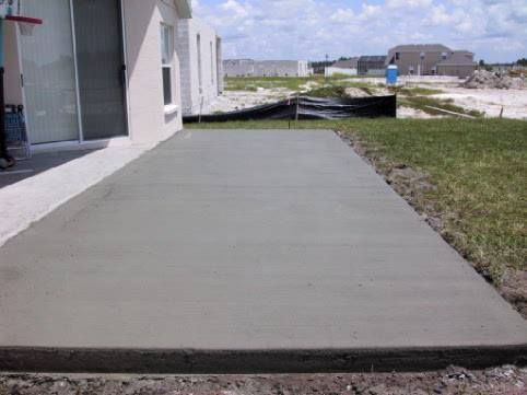 Newly poured concrete patio next to a house under construction.