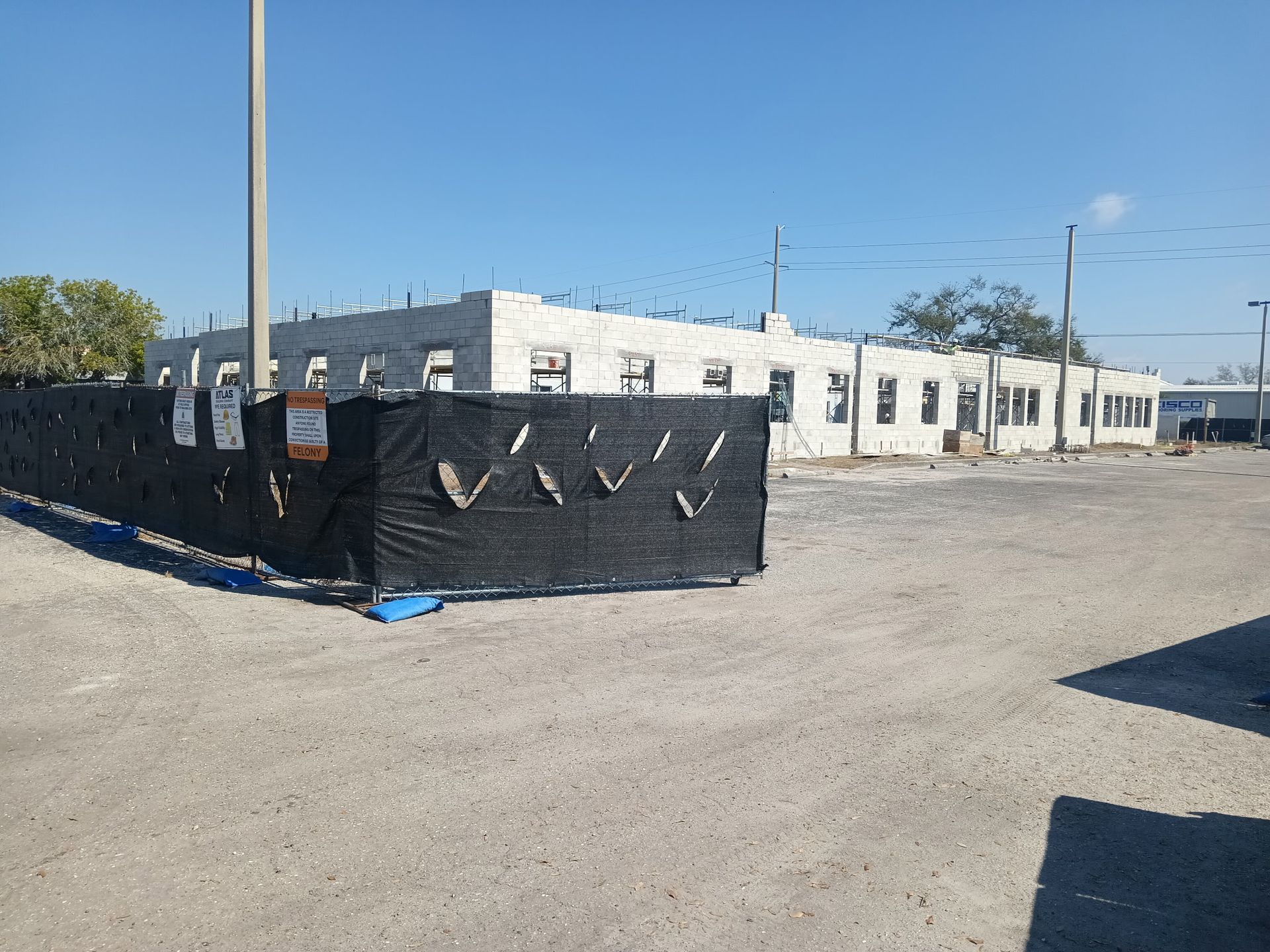 Construction site with cinder block building behind black safety fence. Bright, sunny day.