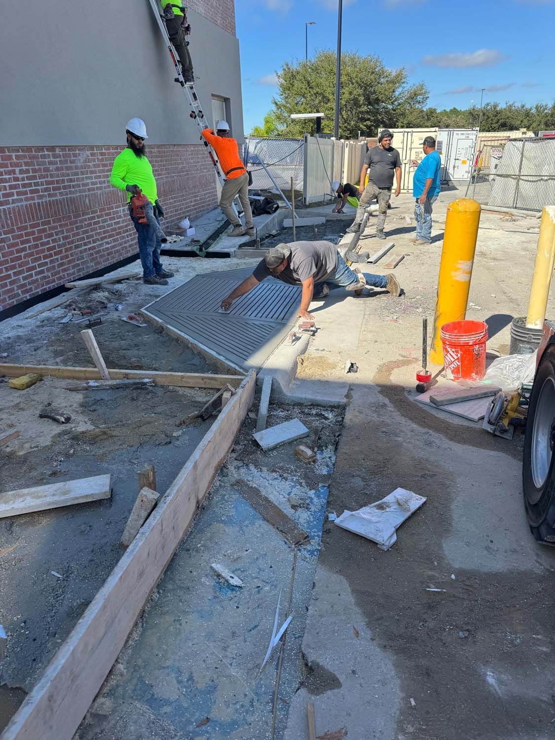 Construction workers installing a metal grate on a concrete surface outside a building under construction.