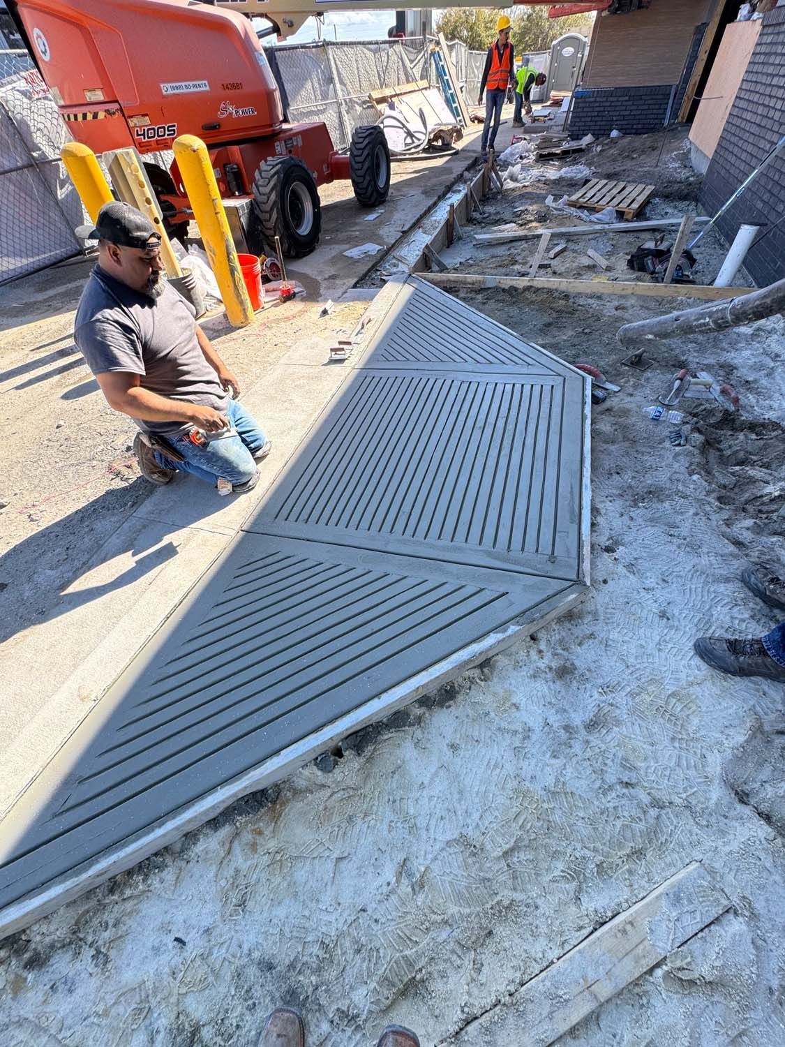 Construction worker kneeling next to large, gray triangular panel with grooved lines, outdoor setting.