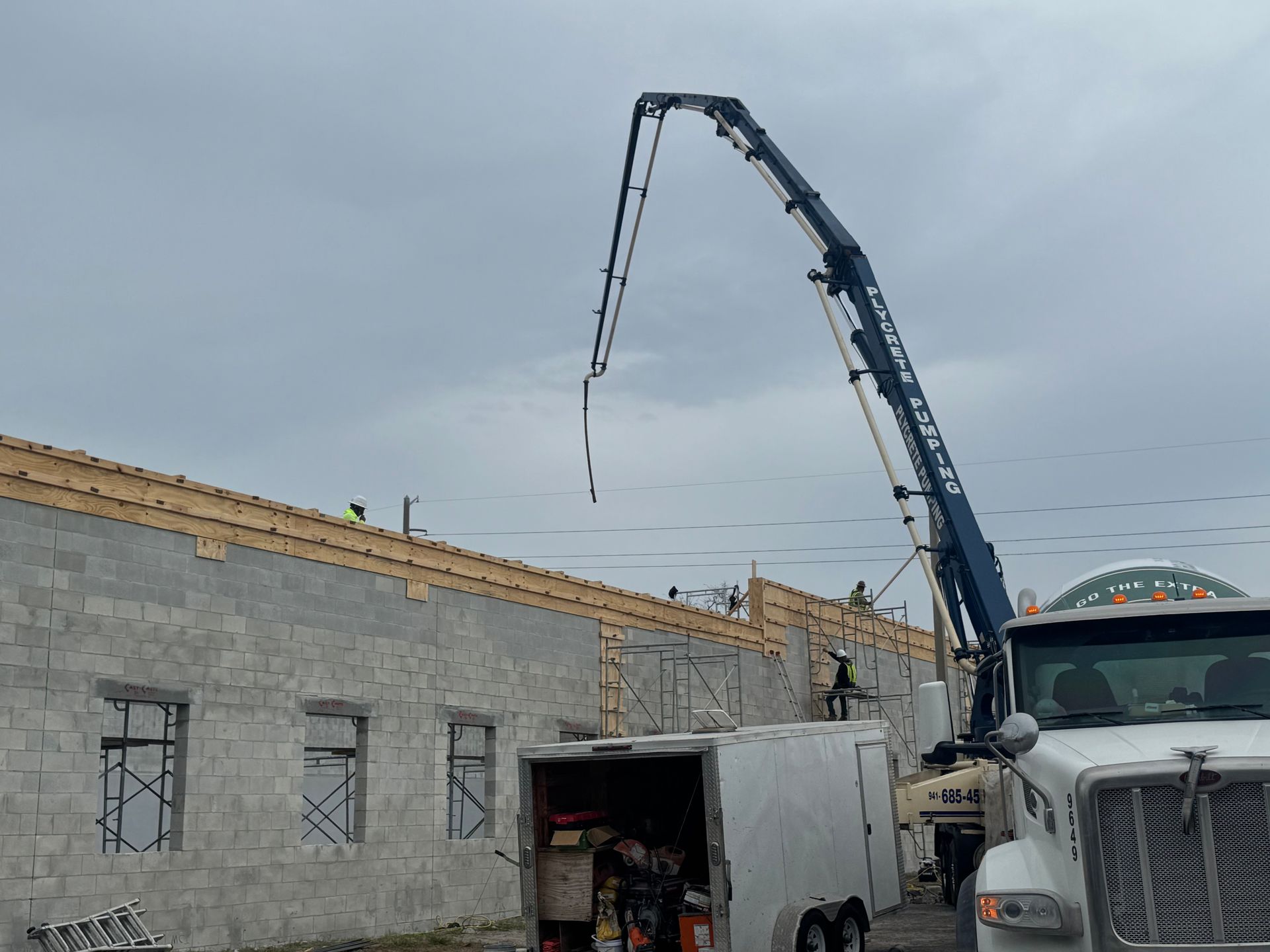 Concrete pump truck pouring concrete onto a building under construction. Cloudy sky.