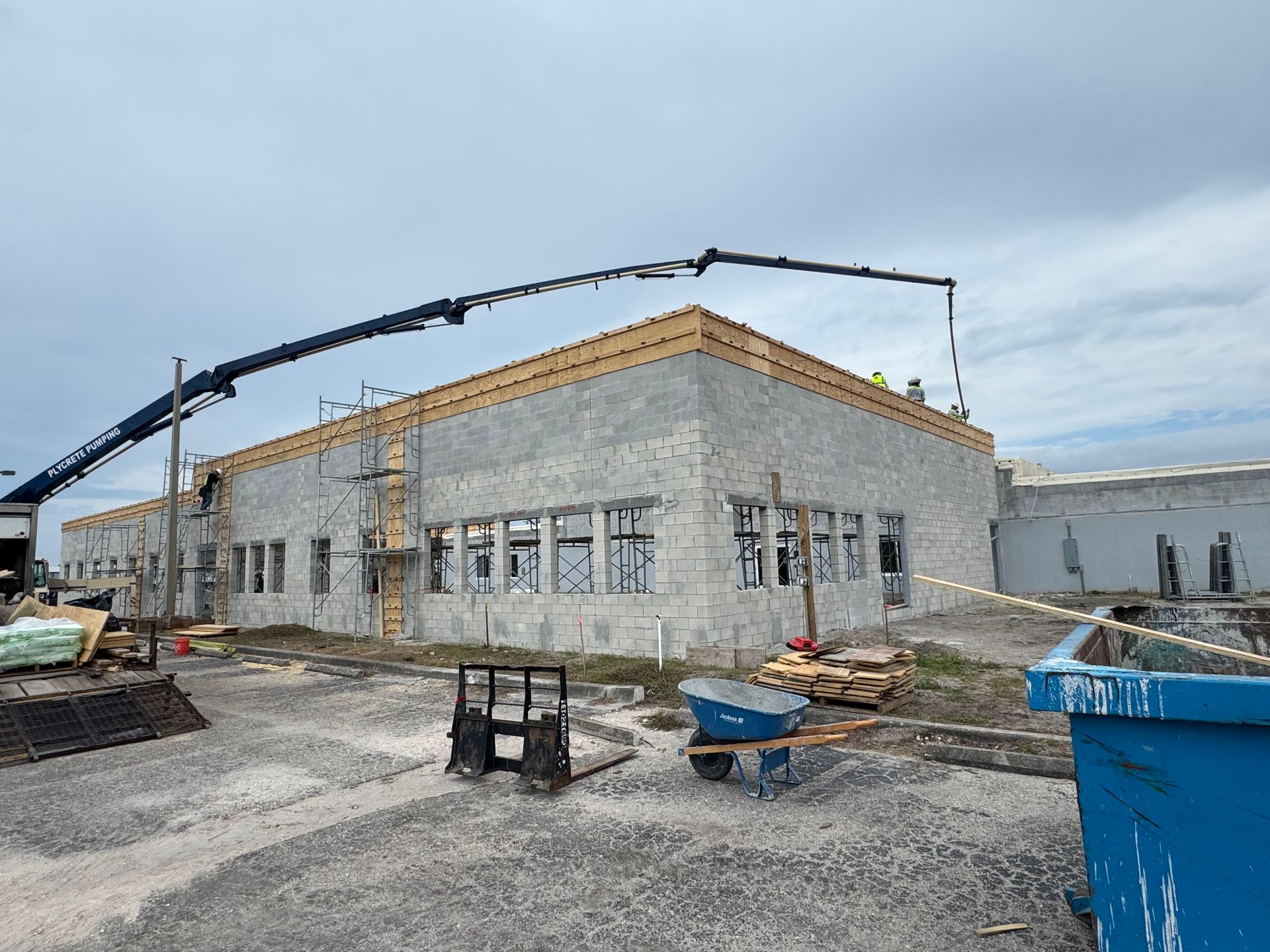 Building under construction with concrete block walls, windows, and a truck parked beside it, under a blue sky.
