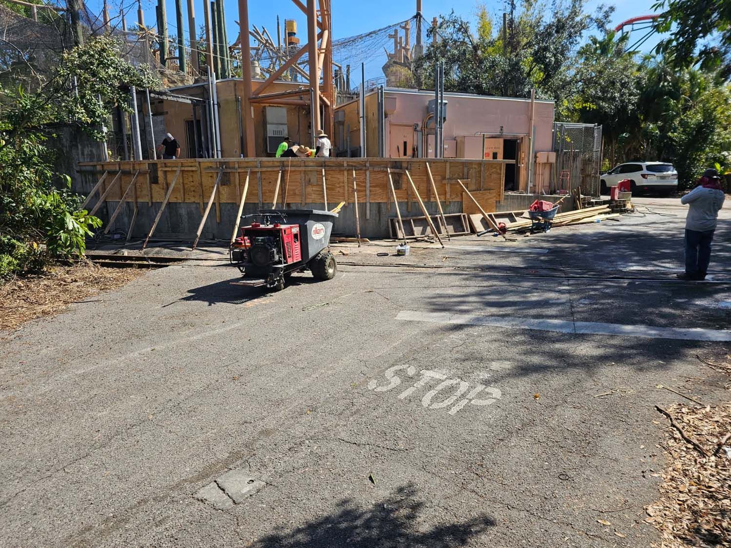 Construction site with workers, wooden framework, and a utility cart on asphalt road. 