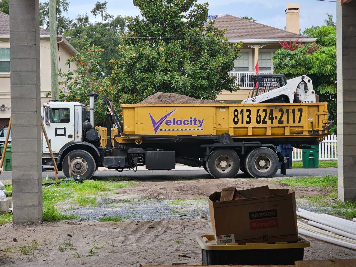 Truck with dumpster filled with dirt, phone number visible. Construction site.