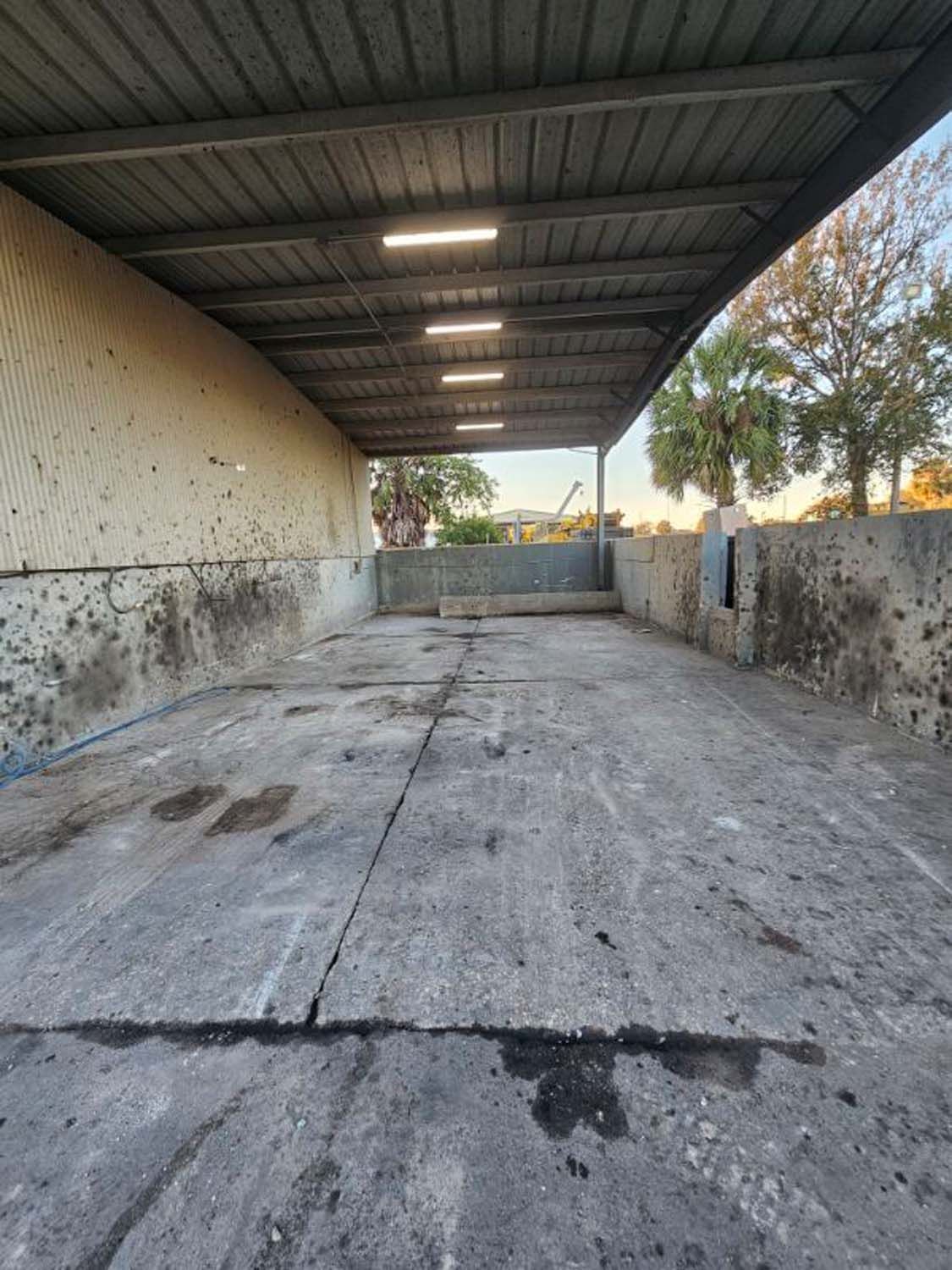 A covered concrete area with lights overhead. The space is empty, with stained walls and floor.