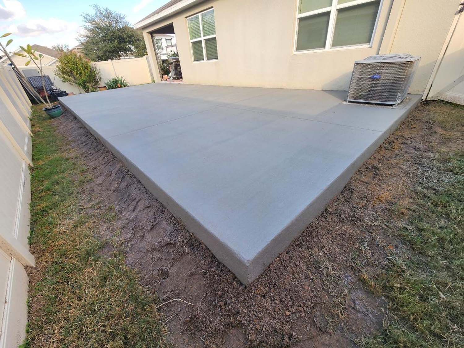 Newly poured concrete patio in a backyard with an AC unit.