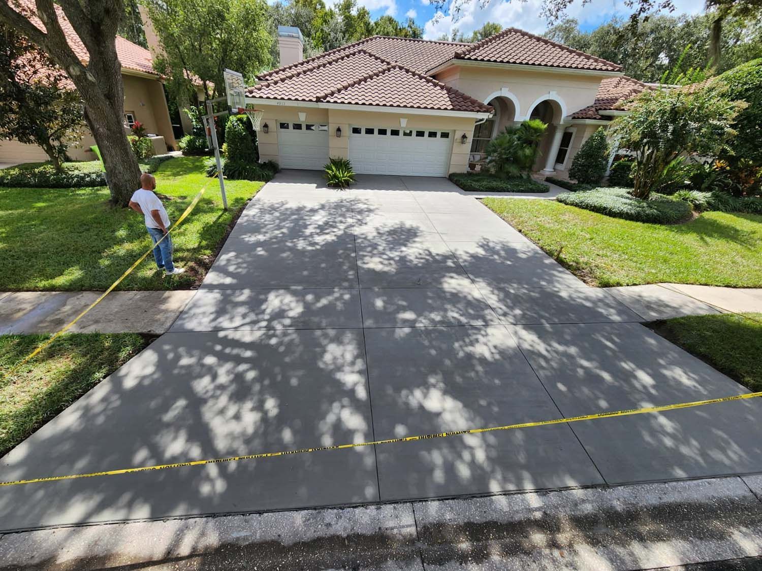 Person measuring a cracked concrete driveway in front of a house with a tiled roof.