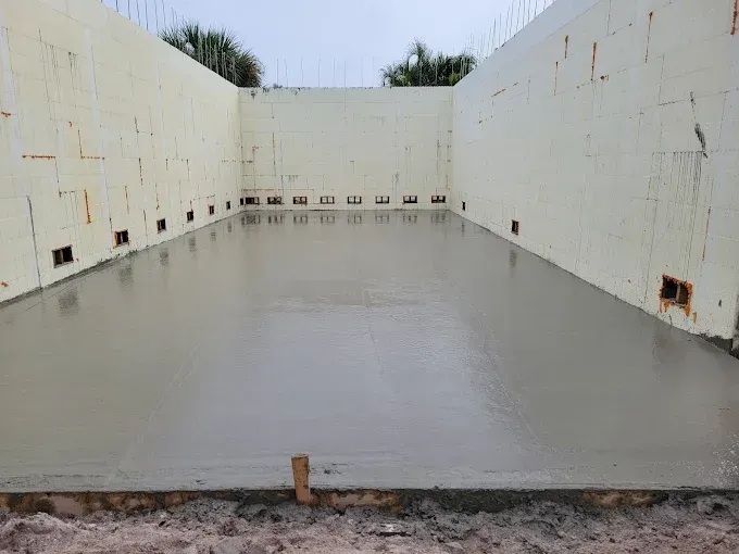 Hands smoothing wet concrete, outdoors. Newly poured, smooth concrete floor within beige insulated concrete form walls.