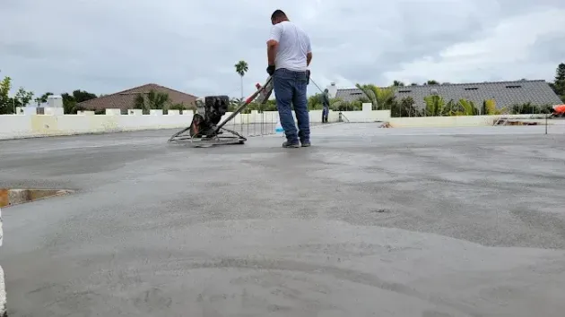 Man using a concrete power trowel on a flat, wet concrete surface outdoors.