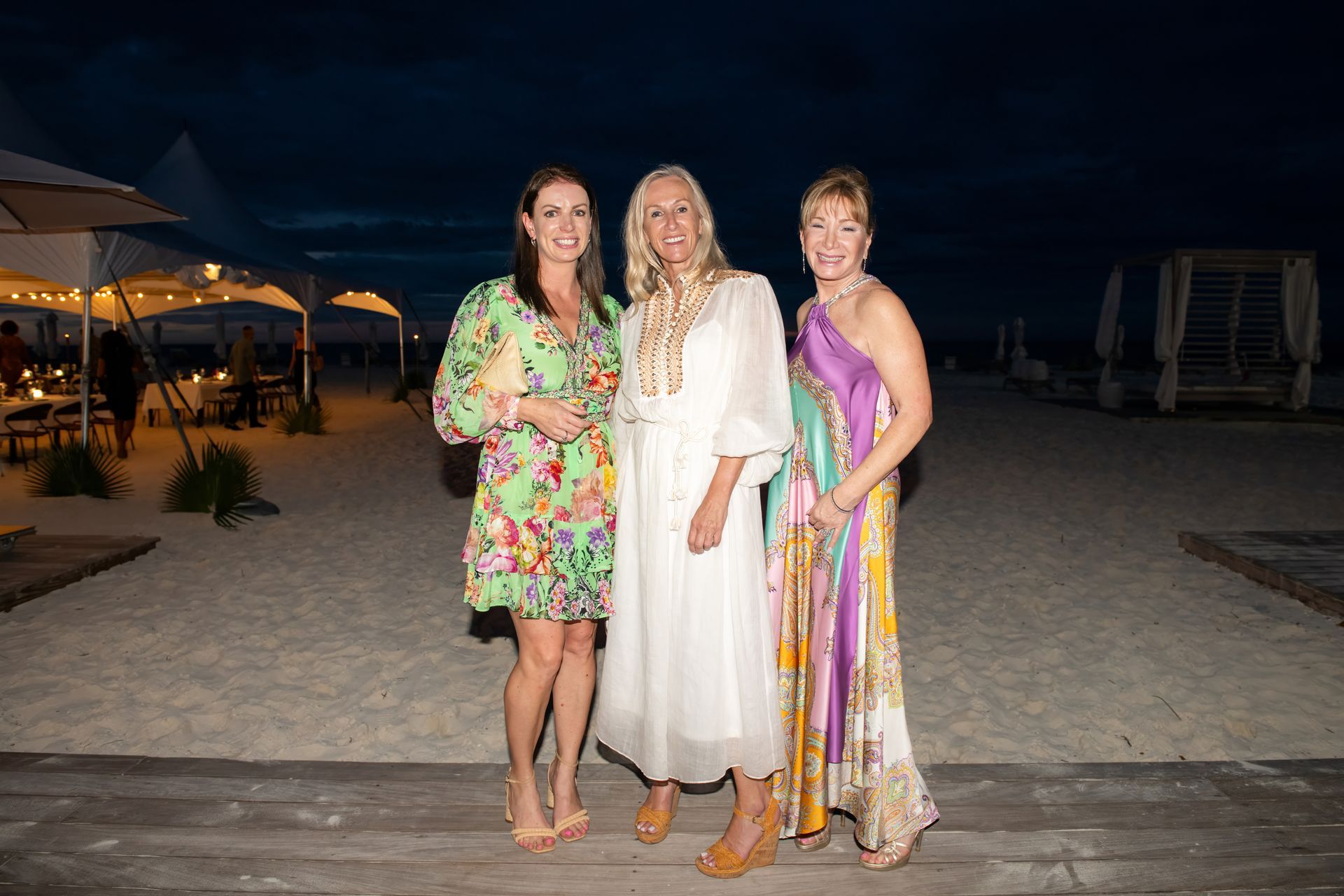 Three women are posing for a picture on the beach at night