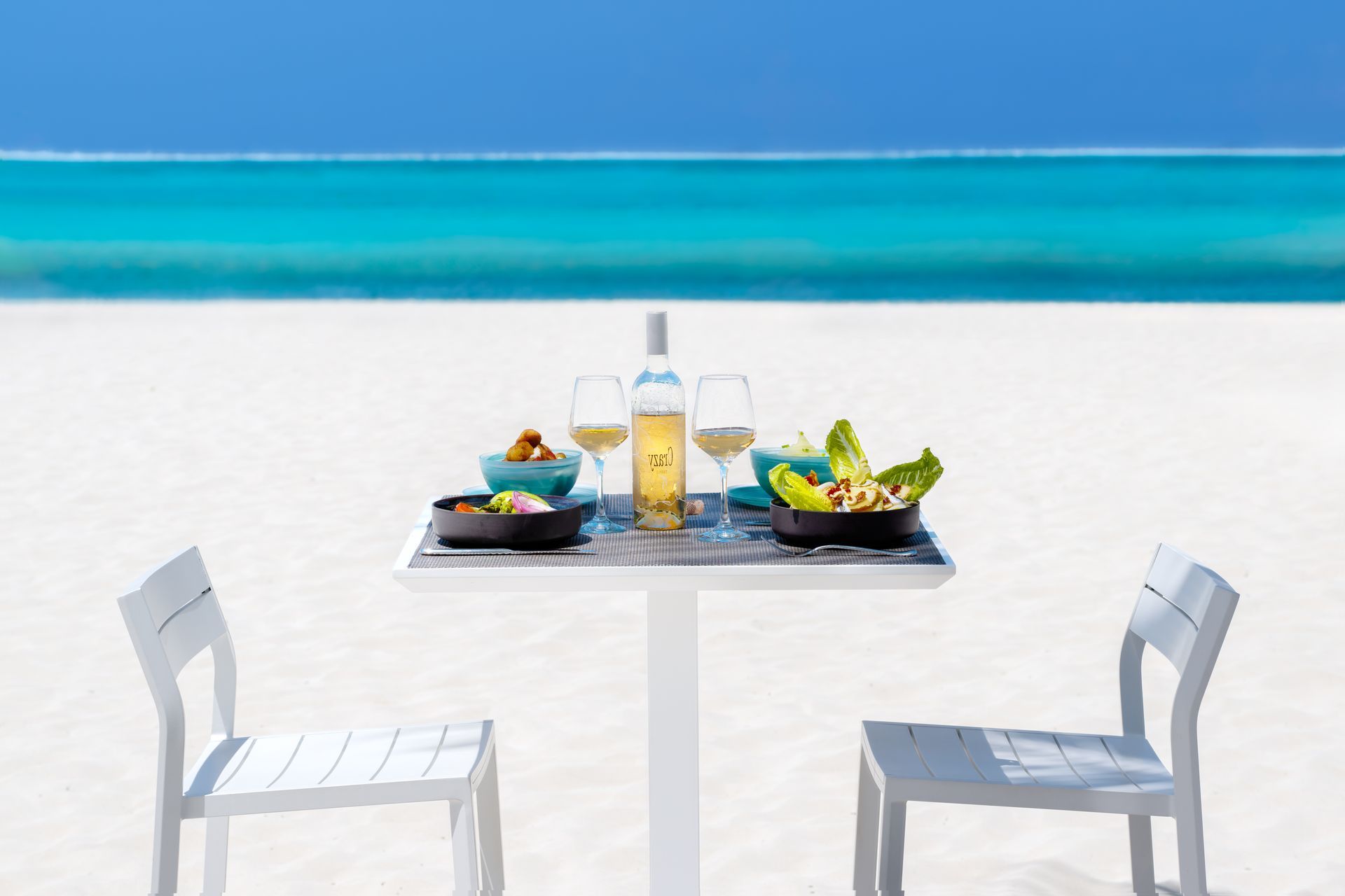 A table on the beach with a bottle of wine on it