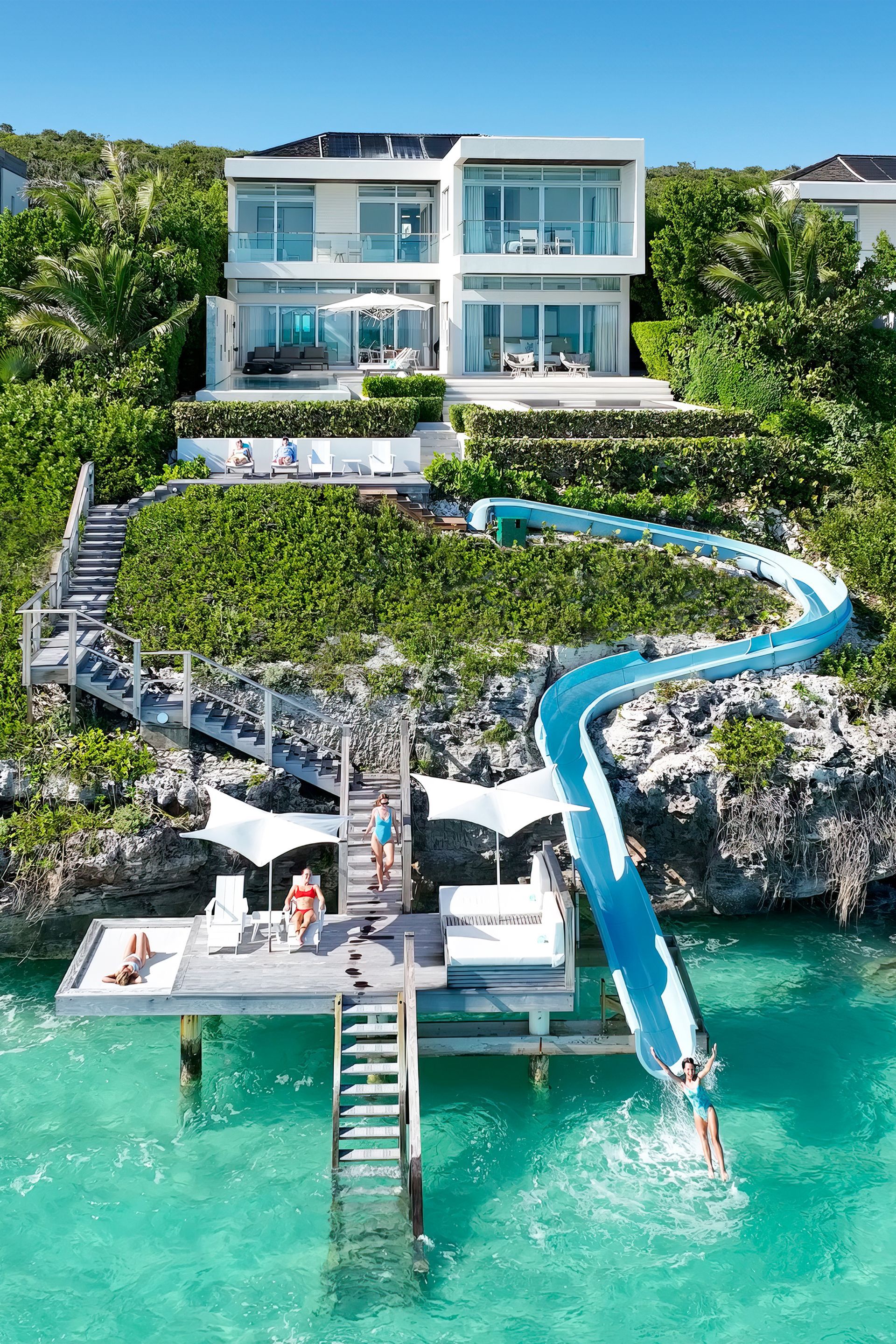 An aerial view of a villa with slide on a cliff overlooking the ocean