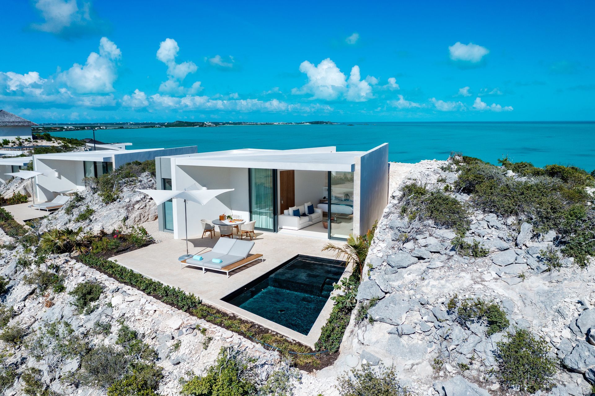 A house with a swimming pool sits on top of a hill overlooking the ocean
