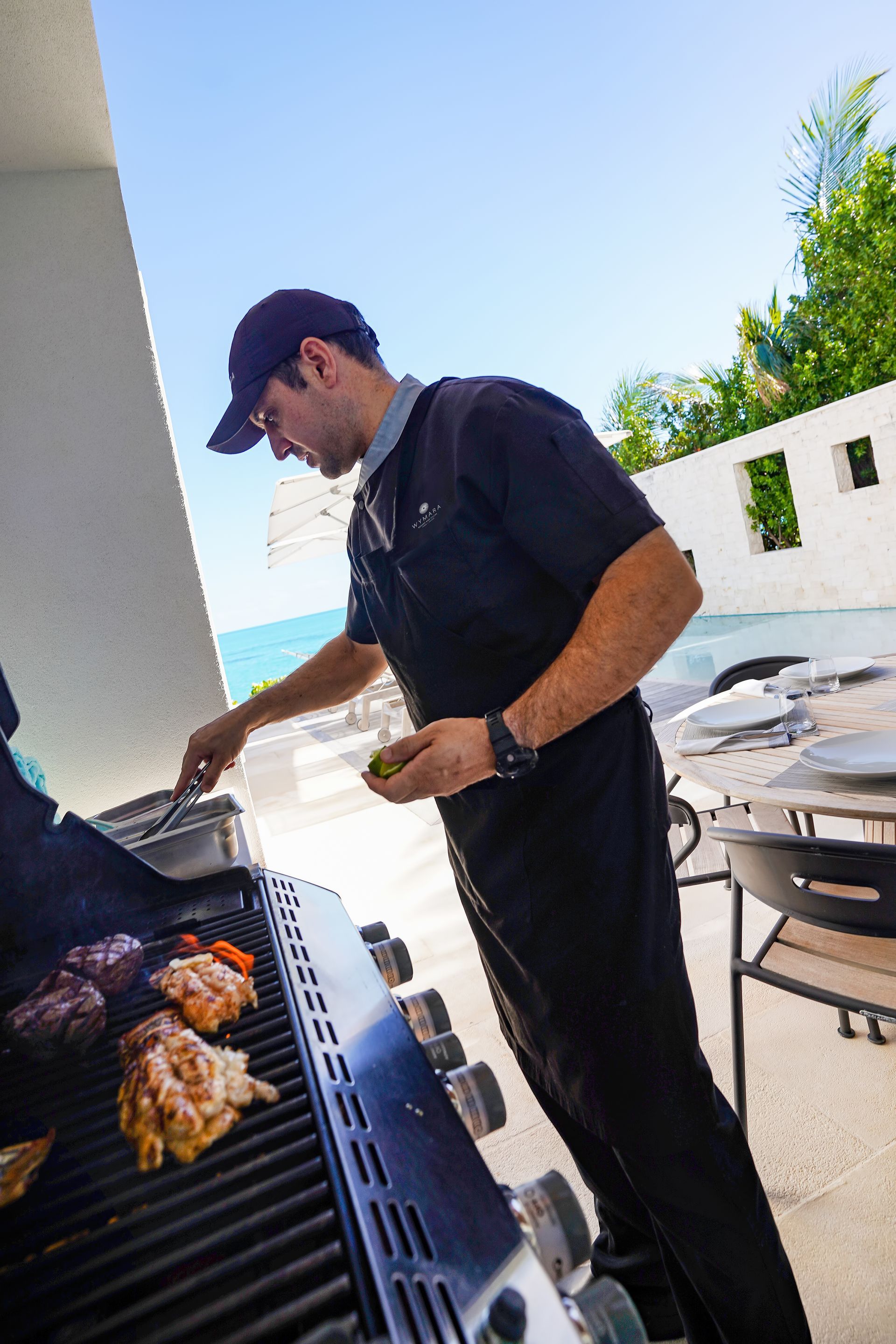 A man cooking on a grill with the ocean in the background