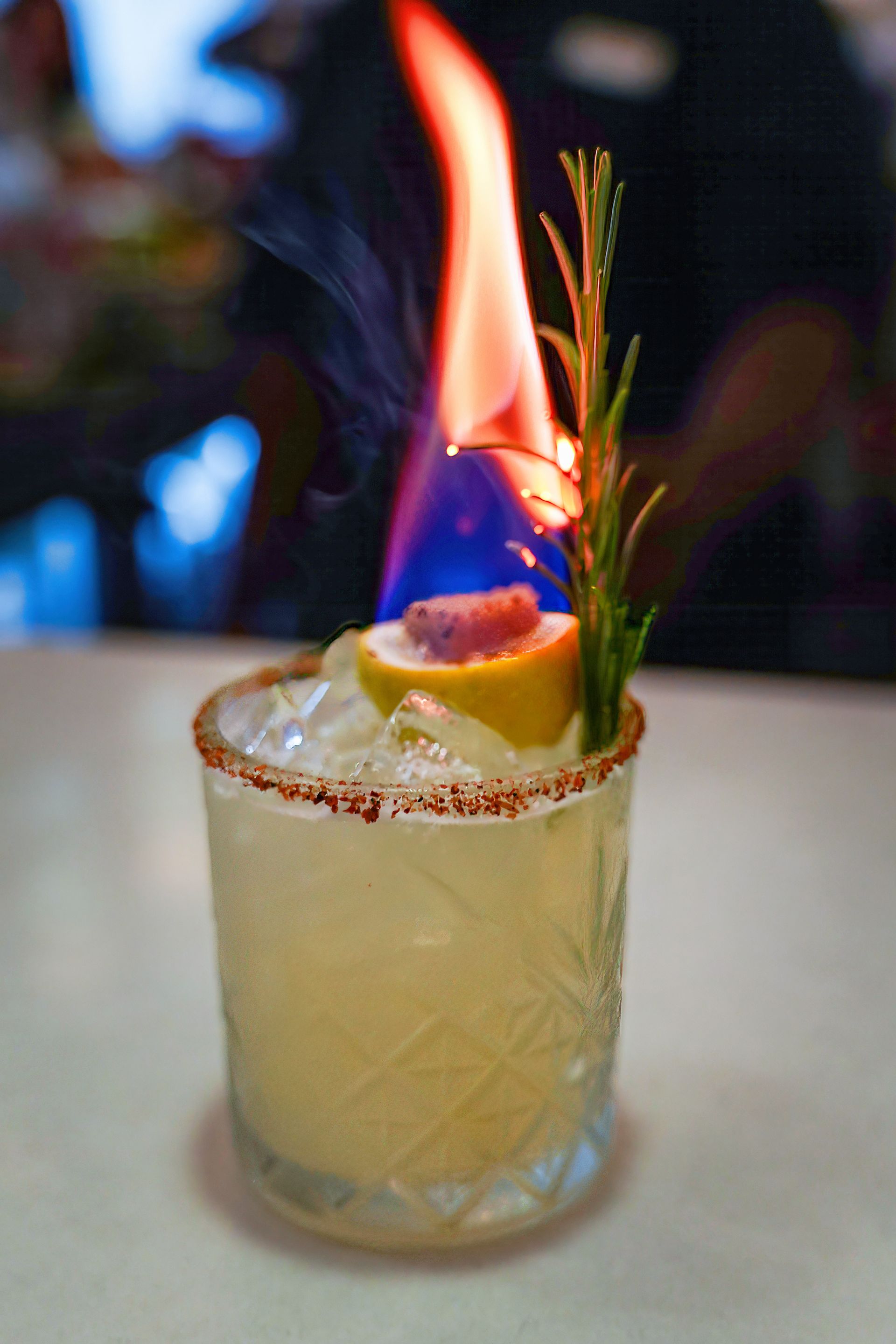 A close up of a drink with a fire coming out of it on a table.