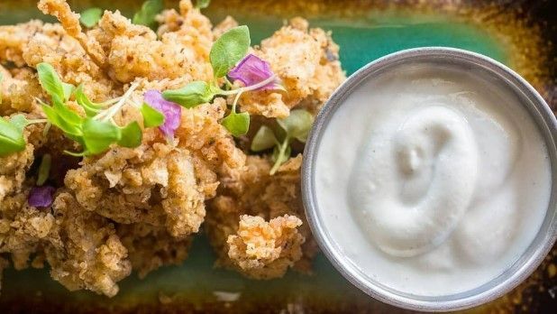 There is a bowl of ranch dressing next to a plate of food.