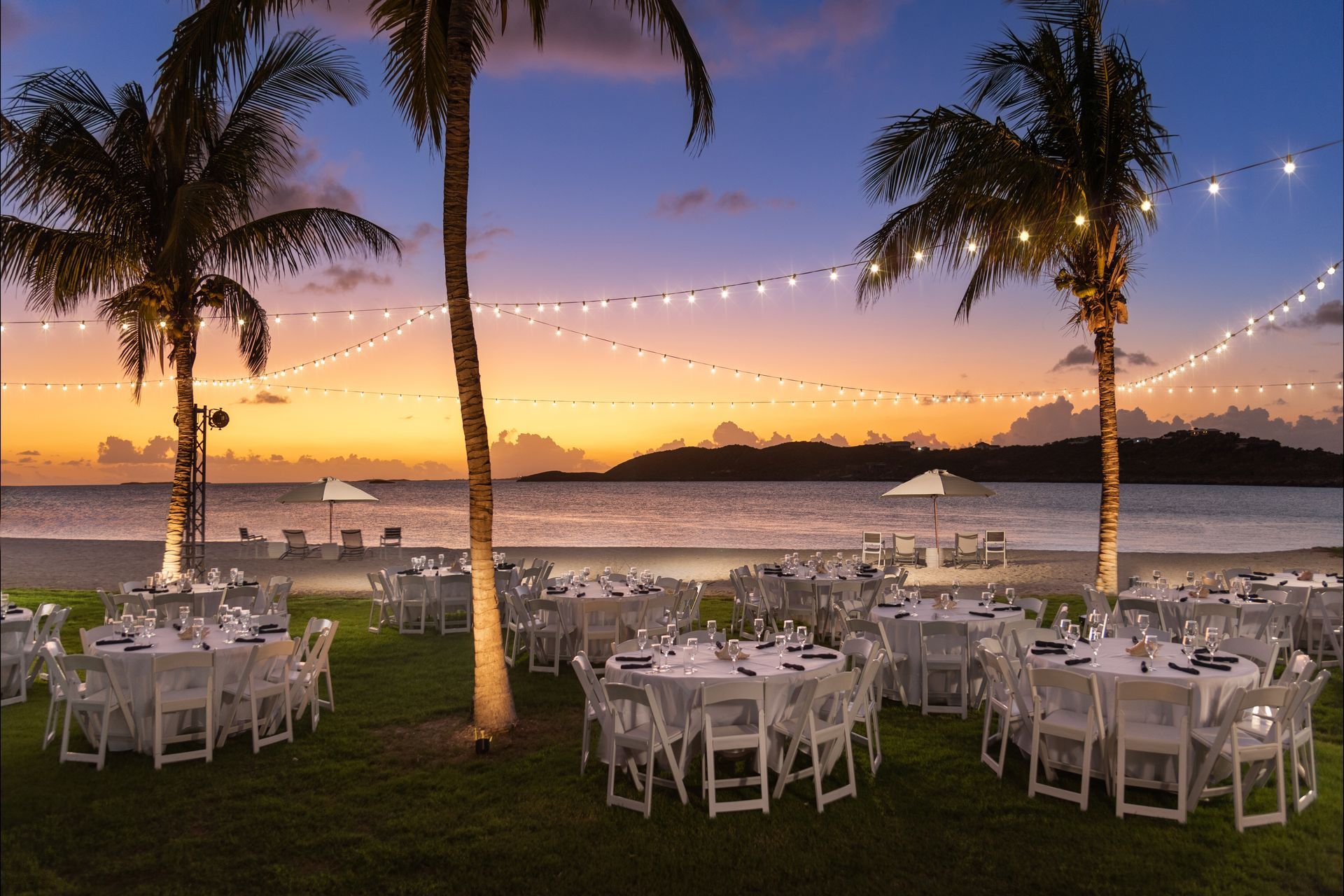 A sunset over the ocean with tables and tents in the foreground