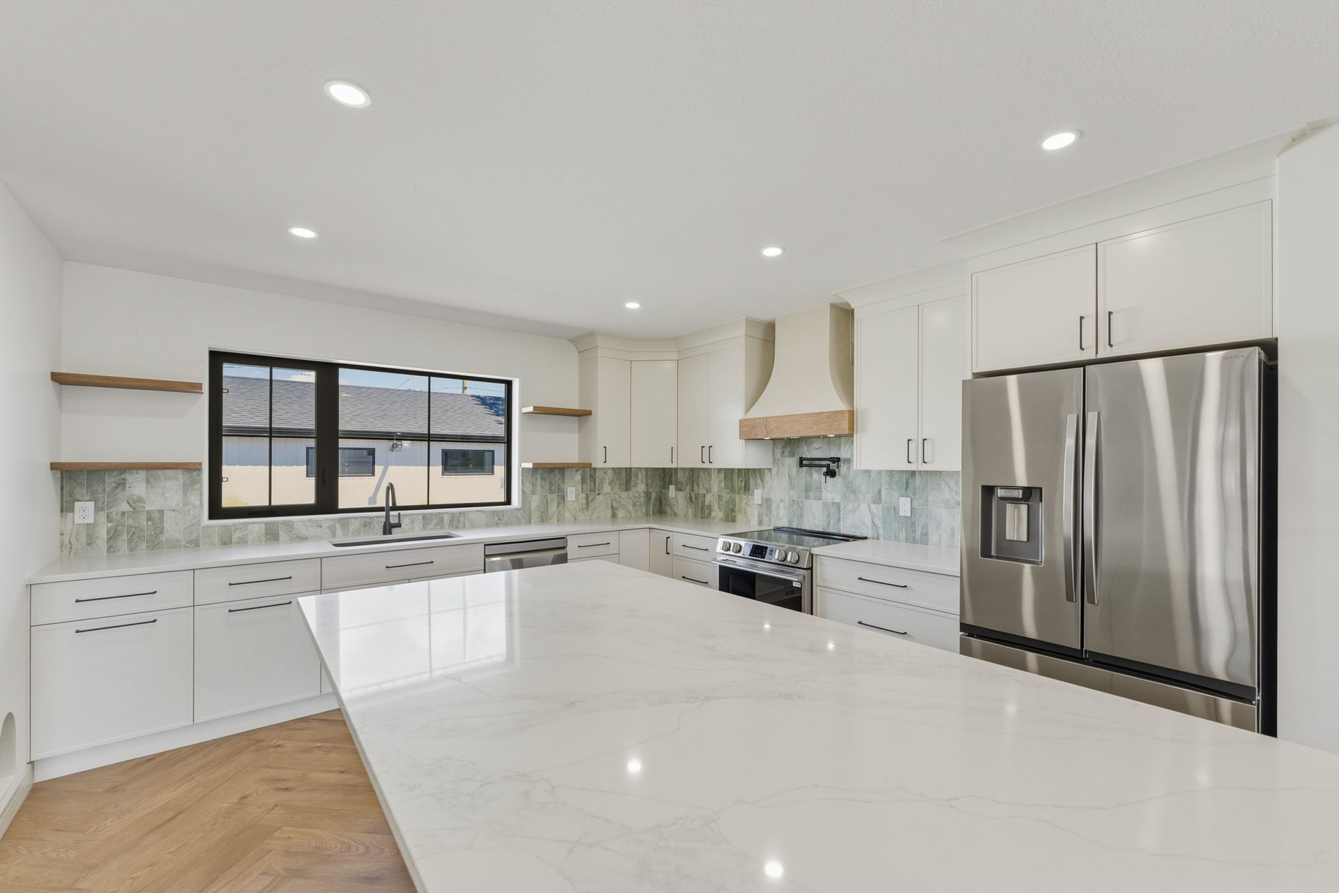 Bright modern kitchen with a large island, white cabinets, stainless steel appliances, and a window over the sink