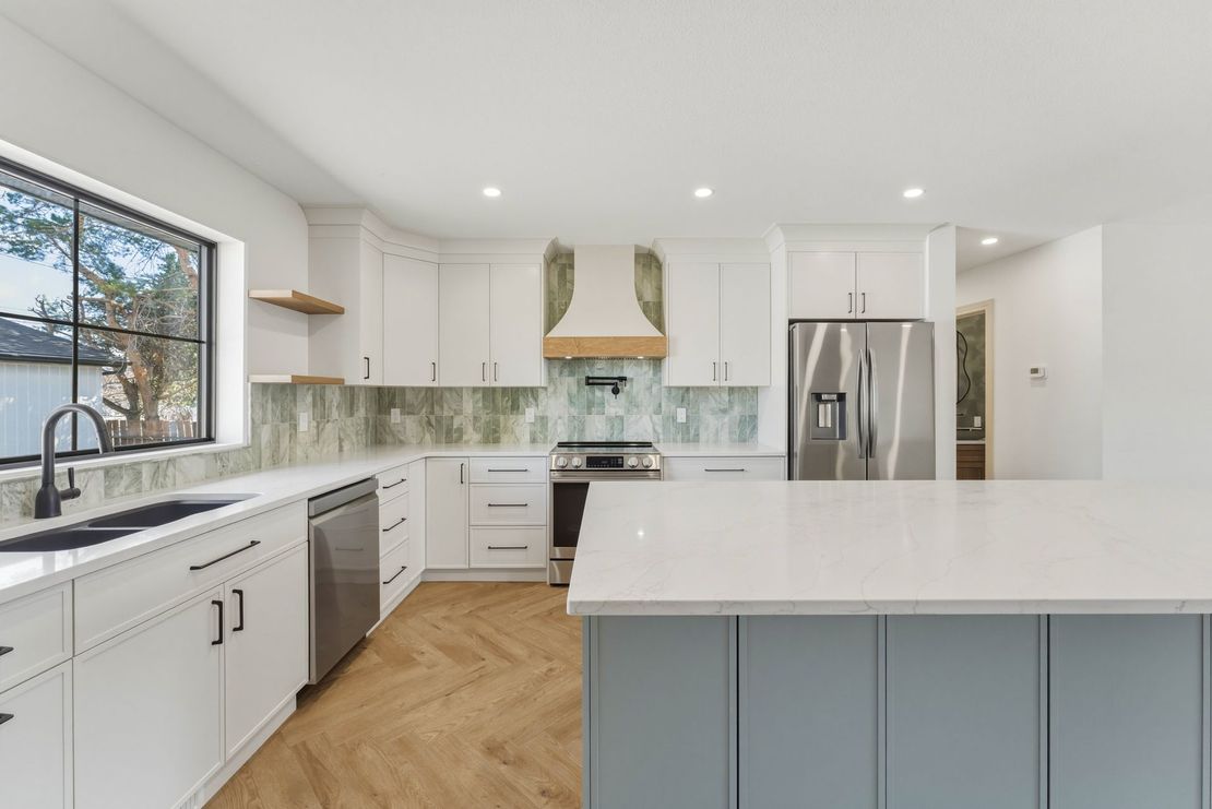 Bright modern kitchen with white cabinets, stainless appliances, large island, and wood herringbone floor