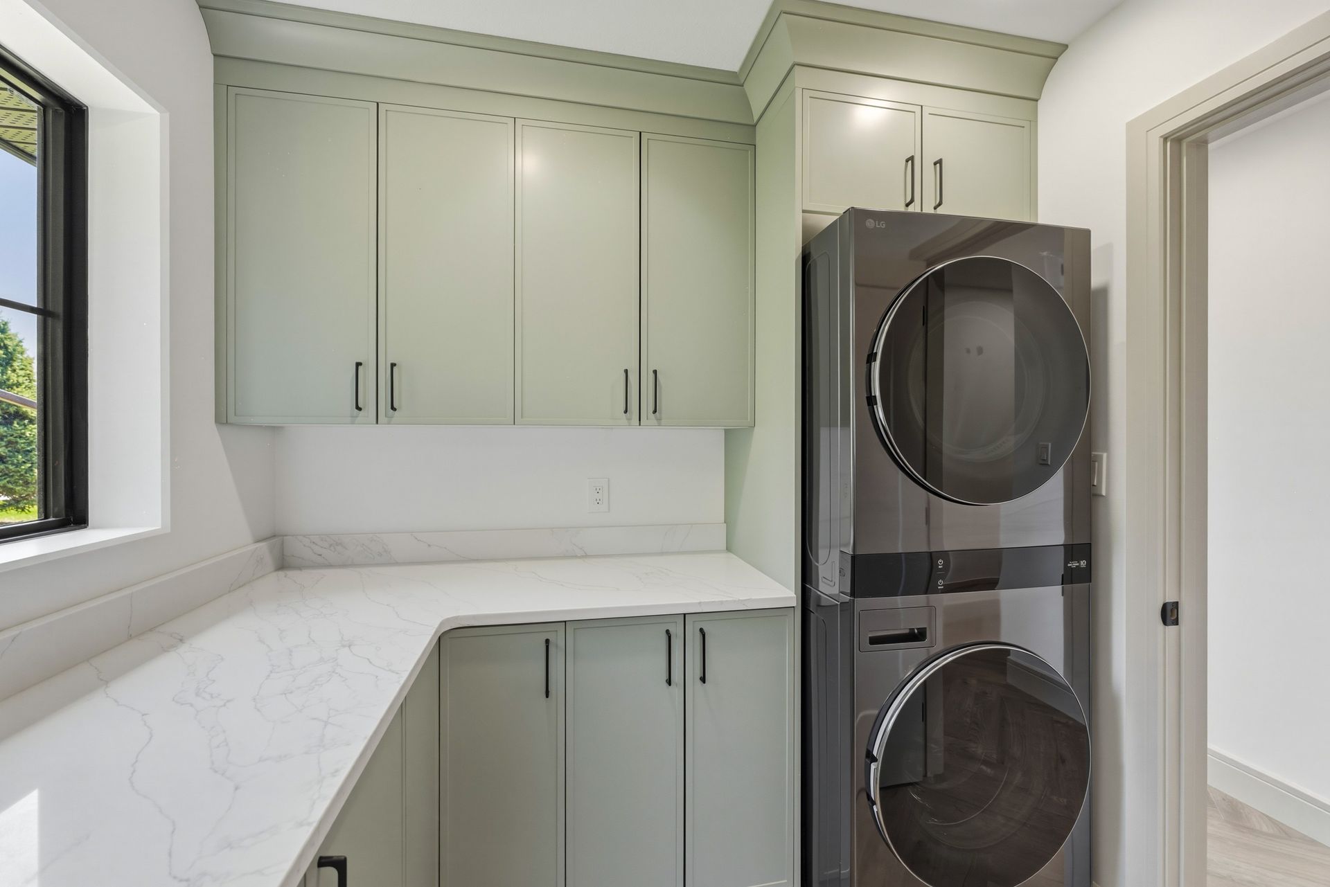 Laundry room with sage green cabinets, white counters, and stacked washer-dryer unit