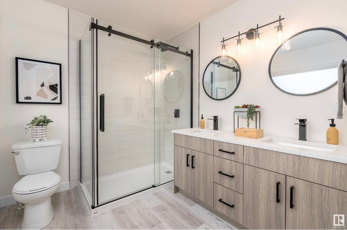 Modern bathroom with glass shower, white toilet, large round mirrors, and wood vanity