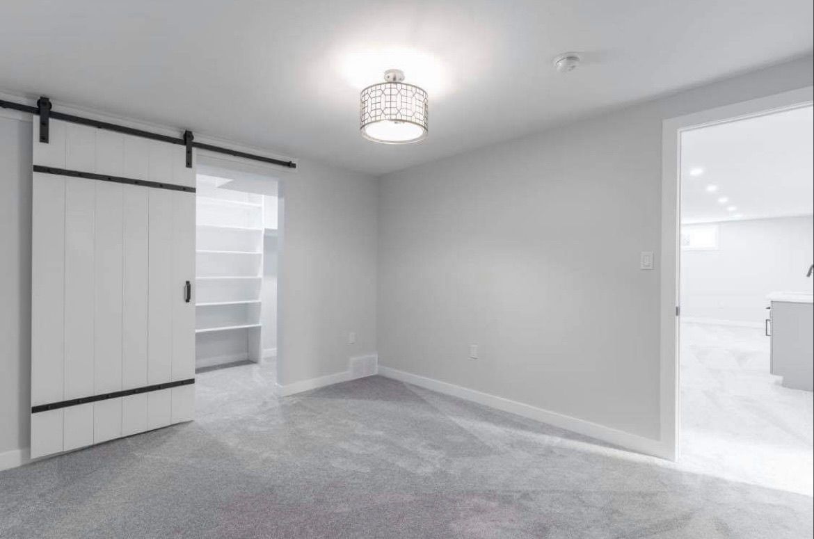 Empty gray bedroom with carpet, closet doors, and an open doorway to a bright adjoining room