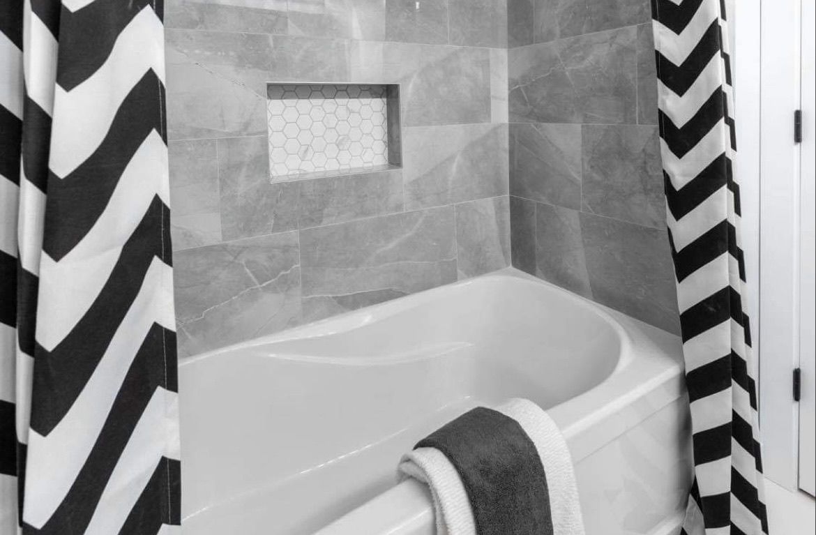 Bathtub with a tiled shower wall, chevron shower curtains, and a towel draped over the tub rim