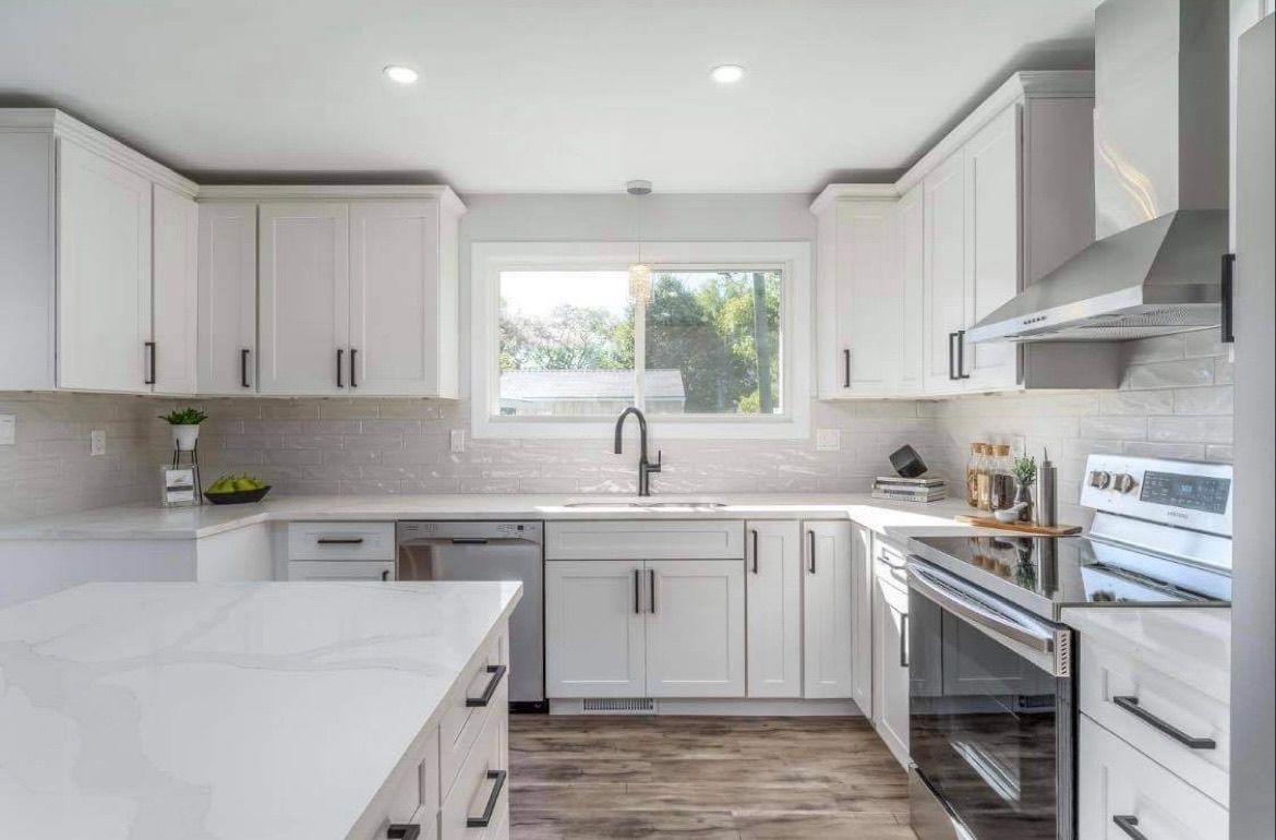 Bright modern white kitchen with island, stainless steel stove, and window above the sink