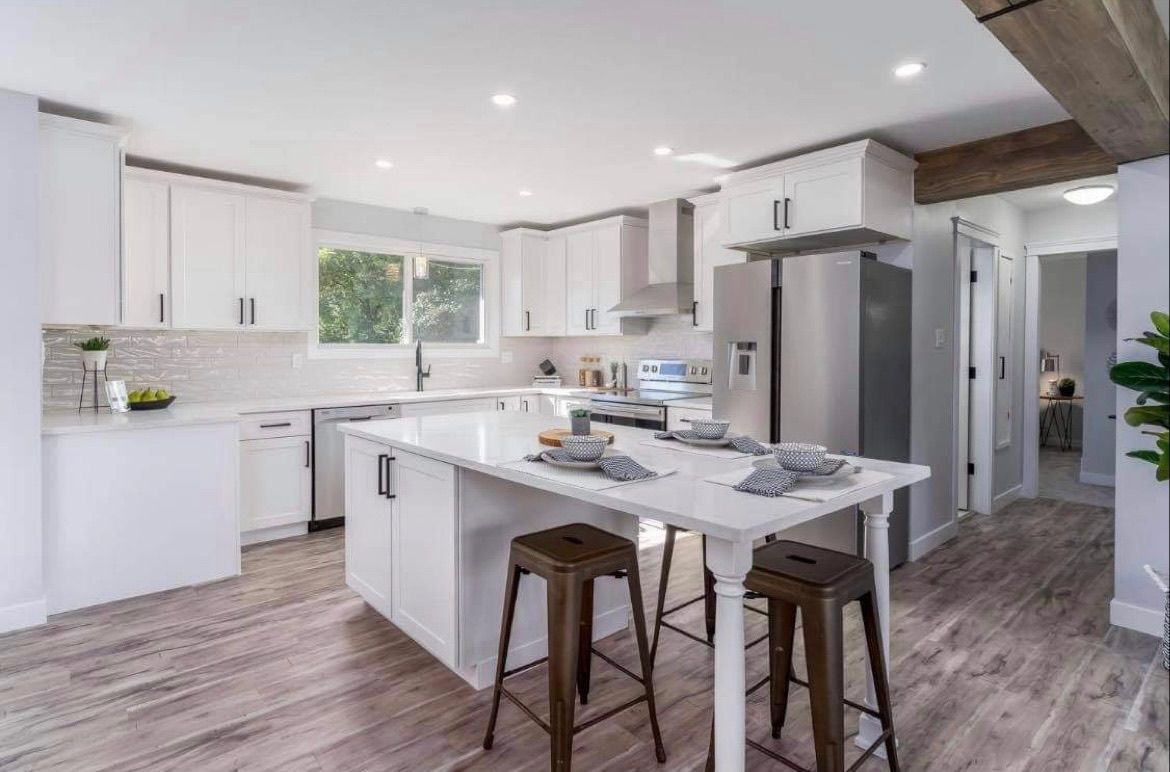 Bright modern kitchen with white cabinets, island, bar stools, and wood flooring
