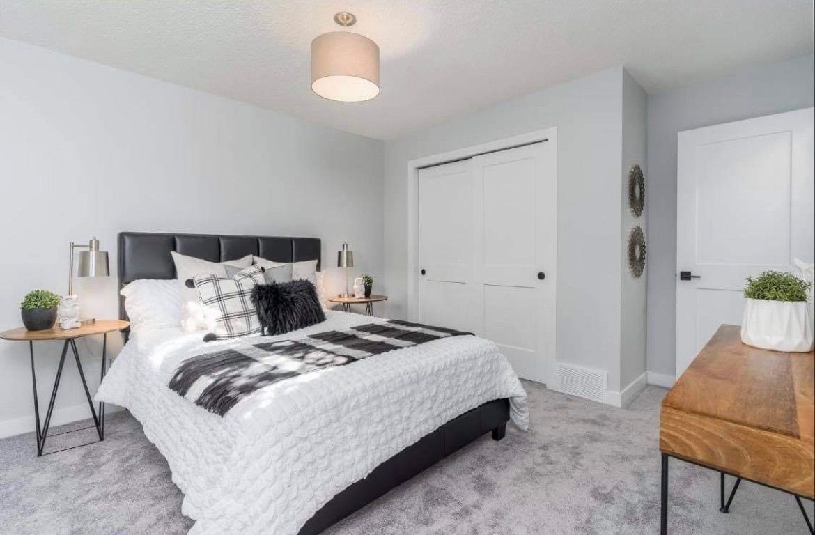 Bright gray bedroom with a bed, wooden desk, white closet doors, and soft neutral decor
