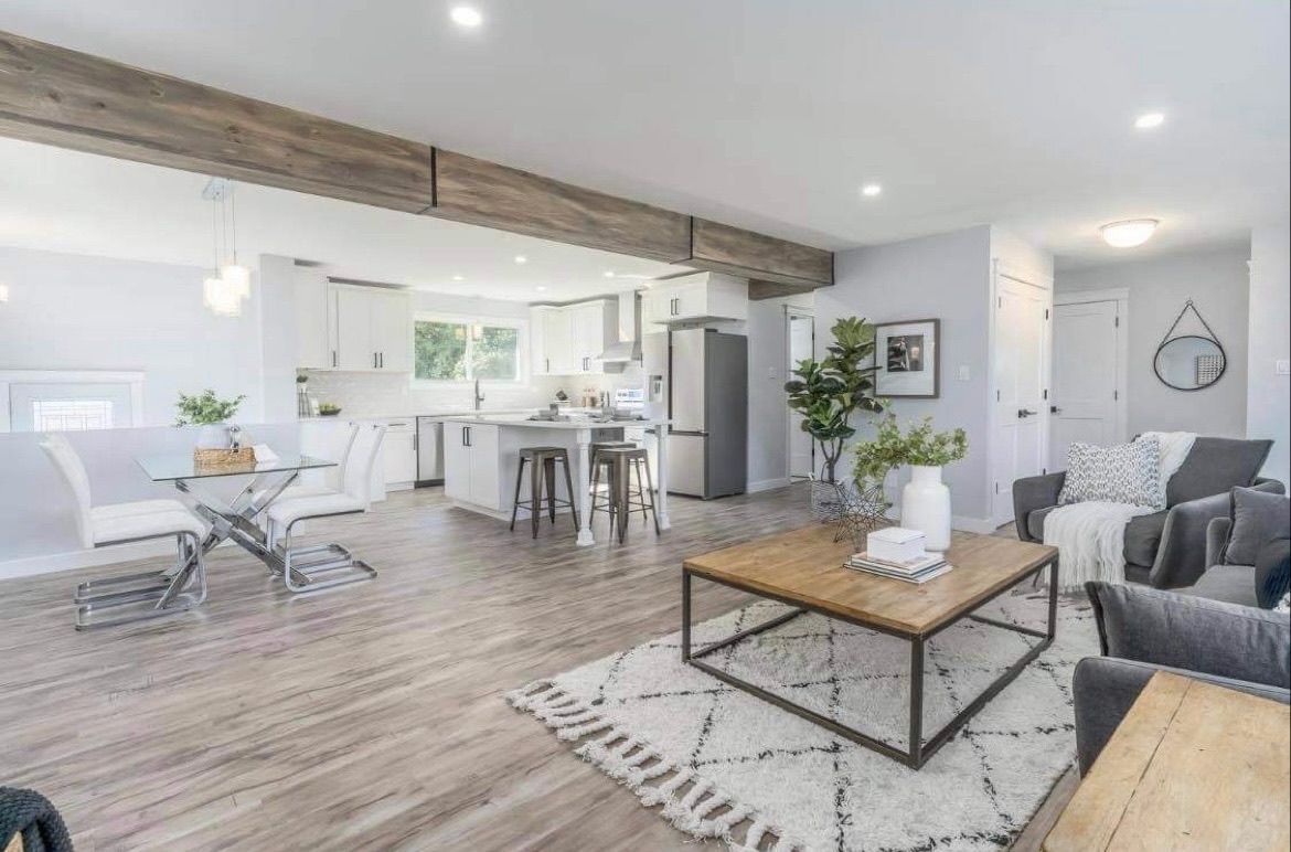 Bright open-plan living room and kitchen with white walls, gray sofa, wood coffee table, and dining area