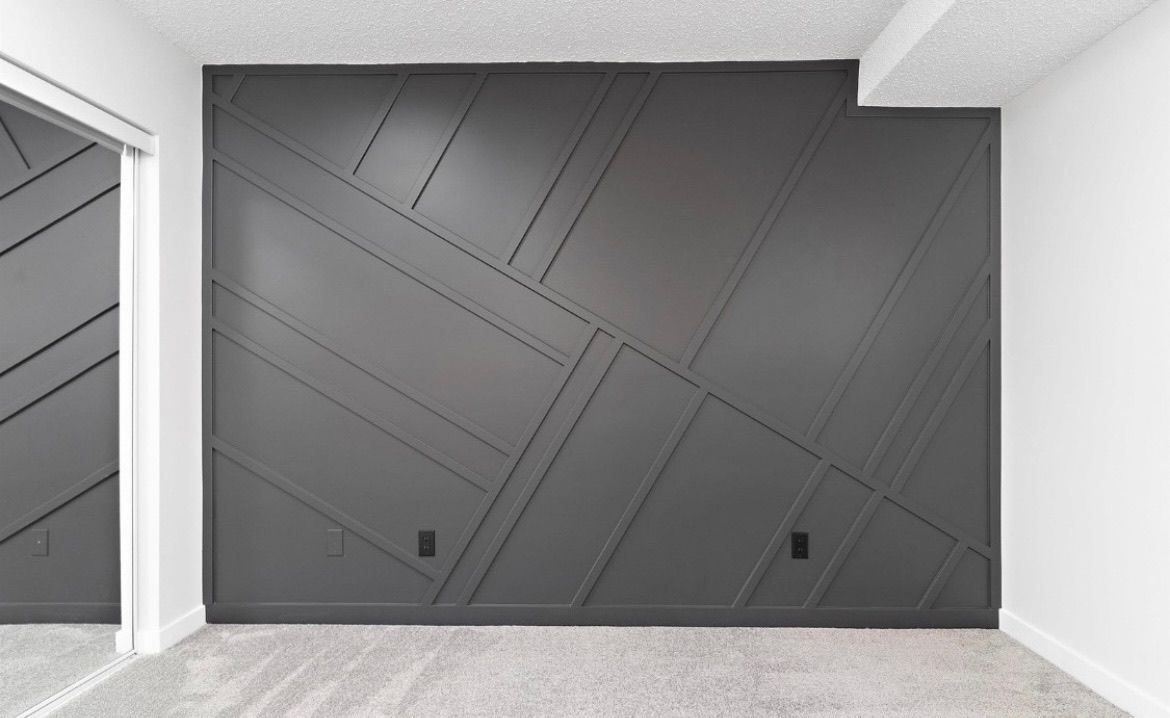 Modern gray accent wall with diagonal lines in a minimalist room with light carpet and white trim