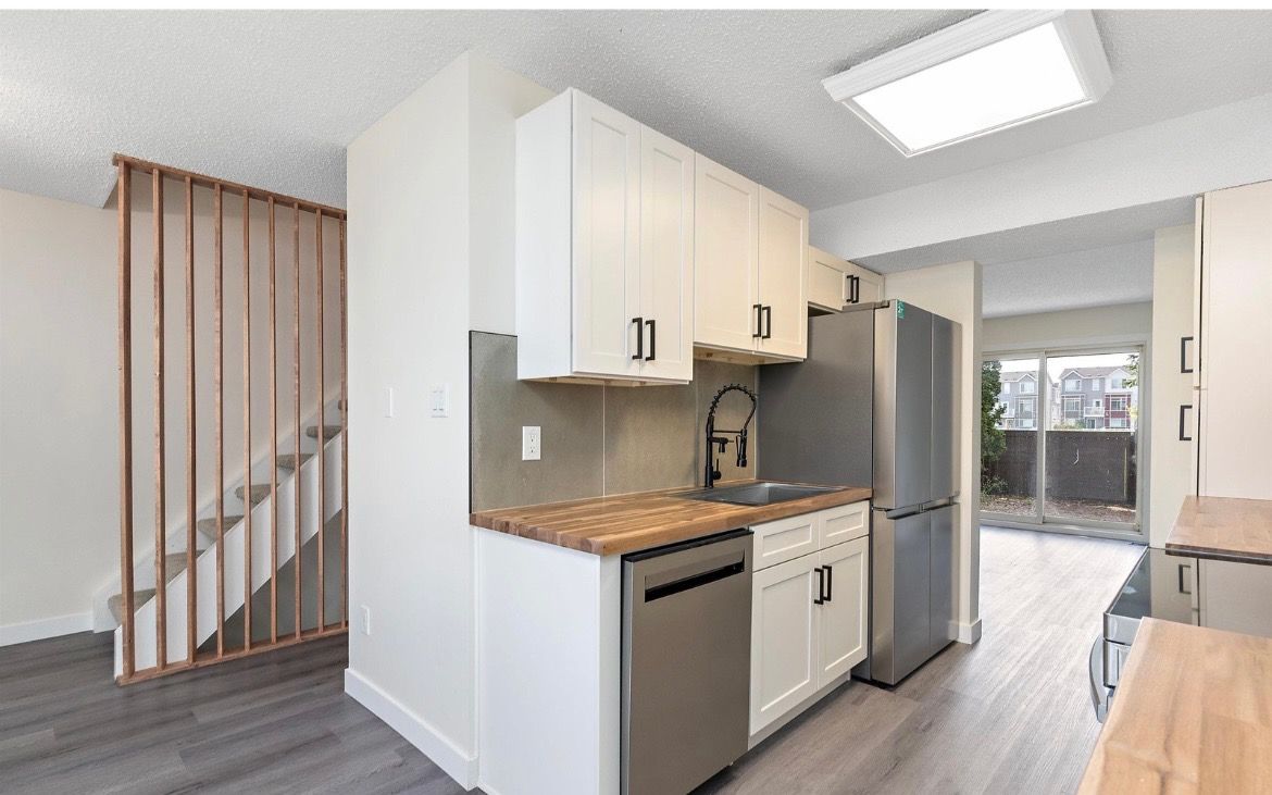 Bright kitchen with stainless appliances, white cabinets, and staircase beside a dining area.