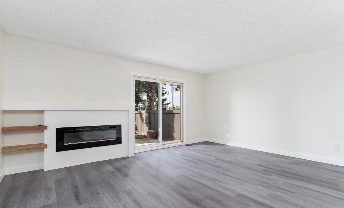 Empty modern living room with white walls, gray flooring, built-in fireplace, and sliding glass door to a patio