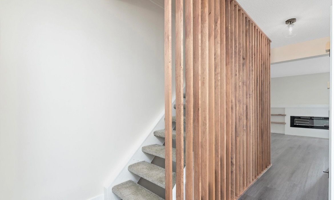 Modern staircase with gray carpet and vertical wood slat partition in a bright interior room
