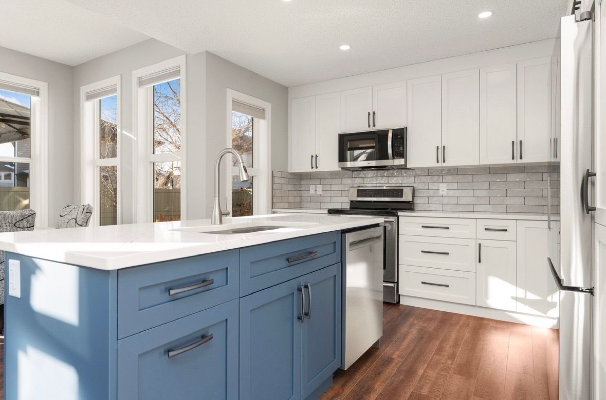 Bright modern kitchen with white cabinets, blue island, stainless appliances, and wood floors
