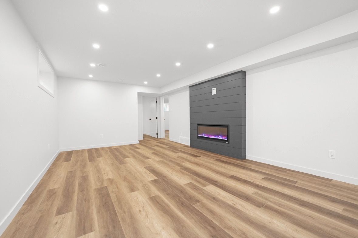 Empty modern living room with white walls, wood floors, recessed lights, and a gray fireplace wall.