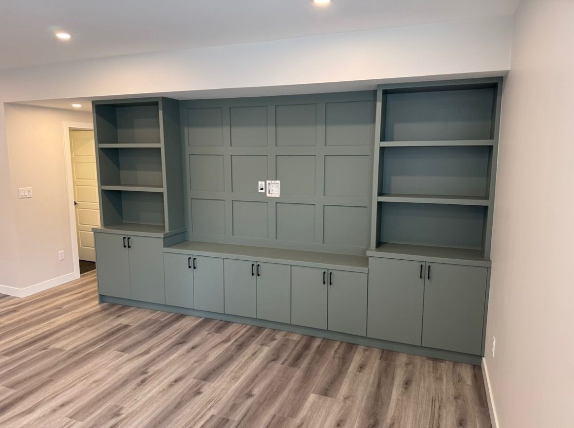 Gray built-in cabinet wall with shelves and lower storage in a bright room with wood floors