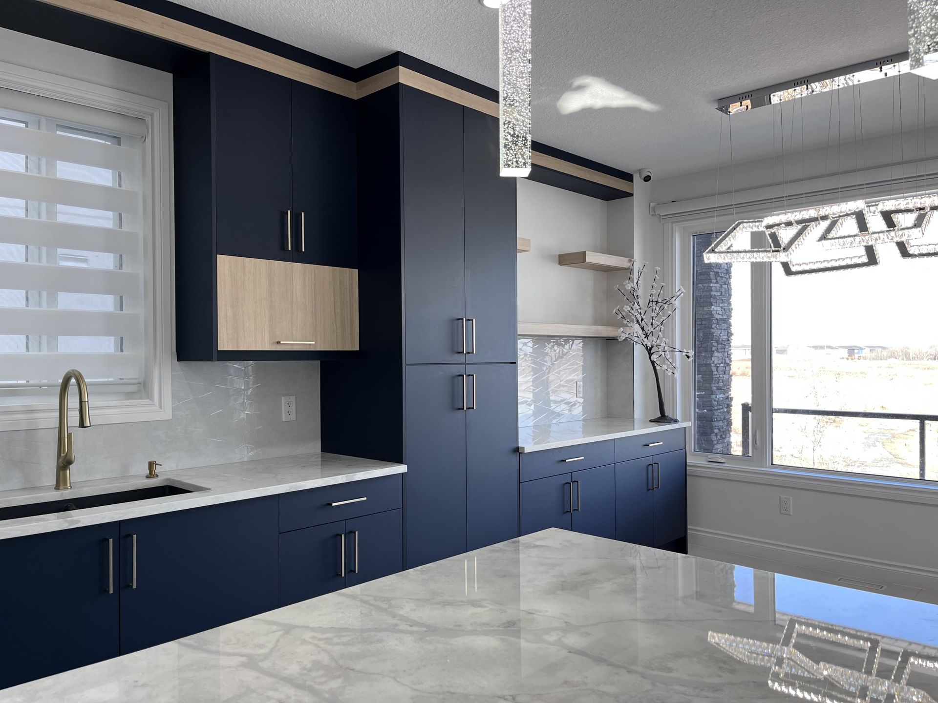 Modern kitchen with navy cabinets, white countertops, and a large window with blinds