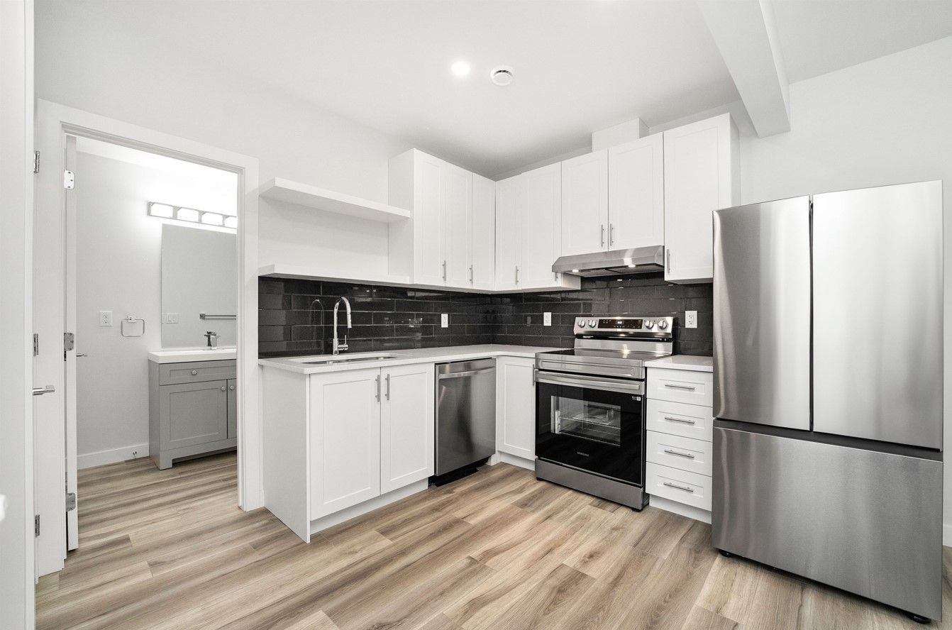 Bright modern white kitchen with stainless steel appliances, black backsplash, and wood-look flooring