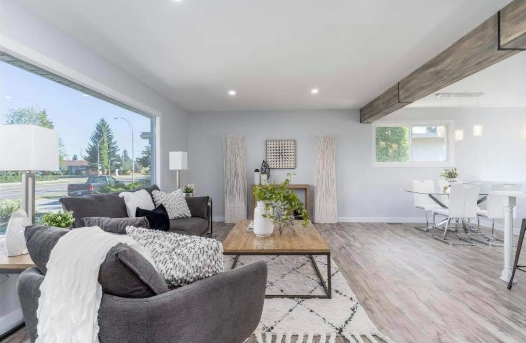 Bright modern living room with gray sofas, wood floor, and dining area by large windows