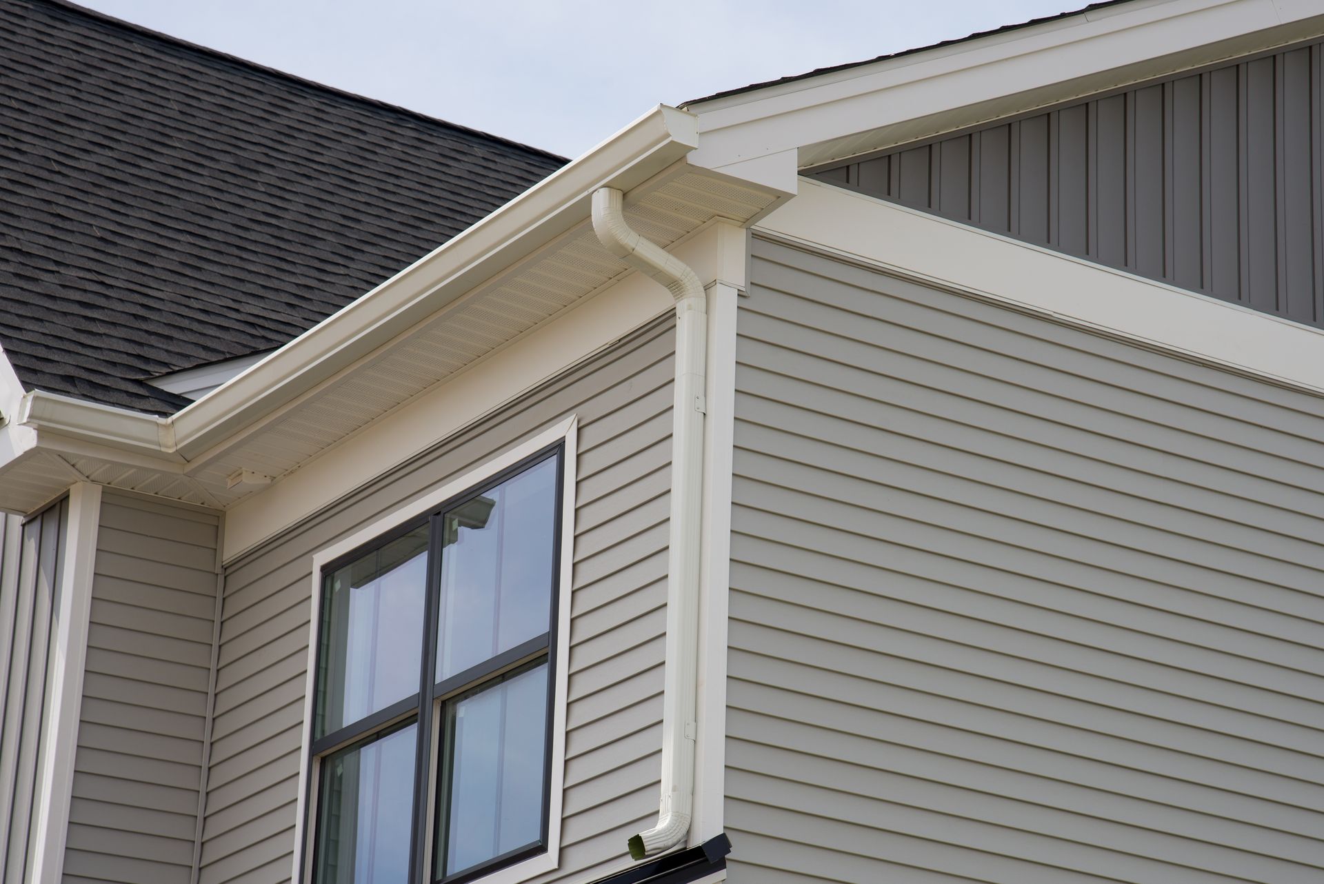 Close-up of a beige house exterior with white trim, a gabled roof, and a large window