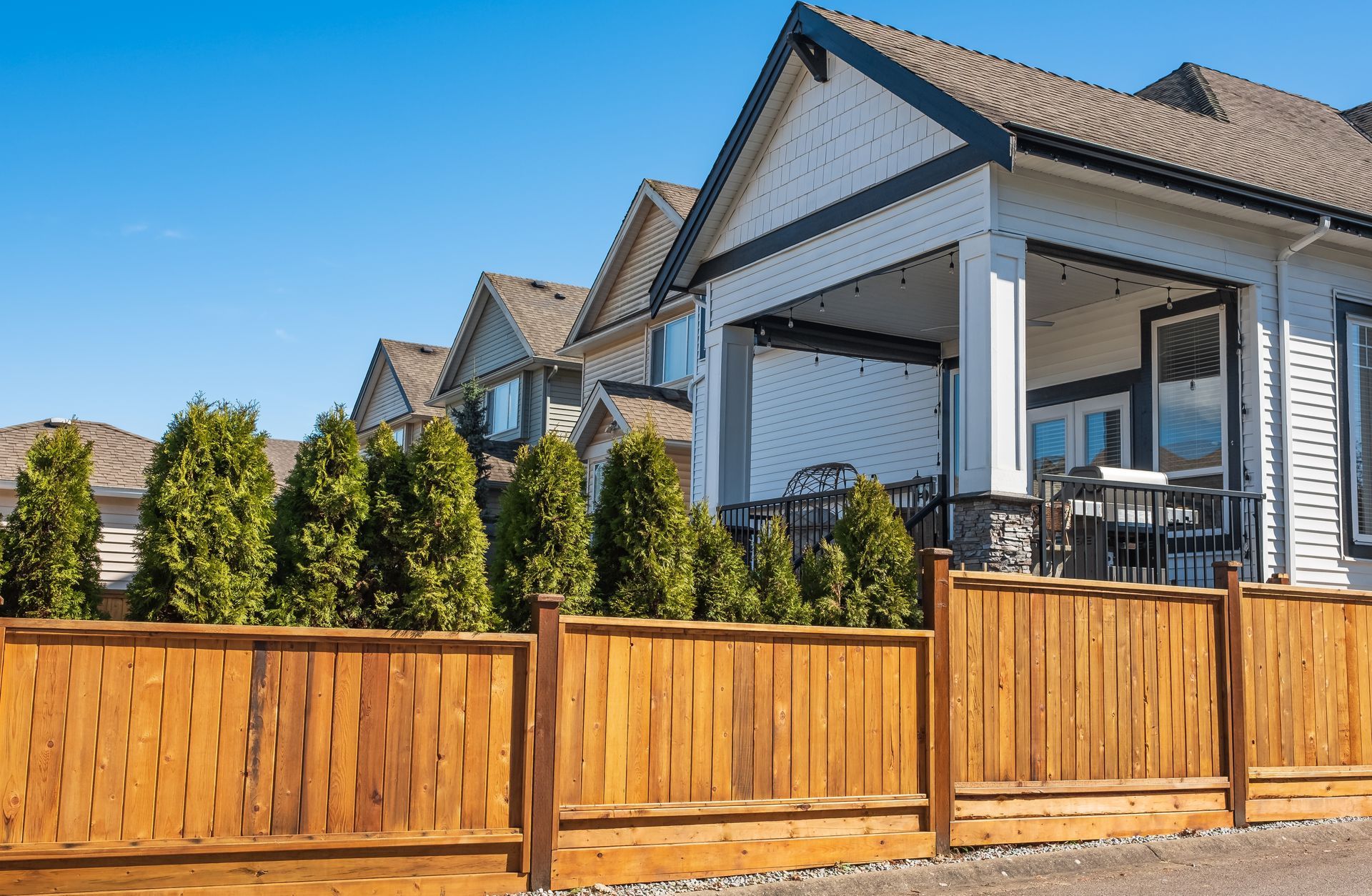 Modern house with a wooden fence, trimmed evergreens, and a sunny front yard