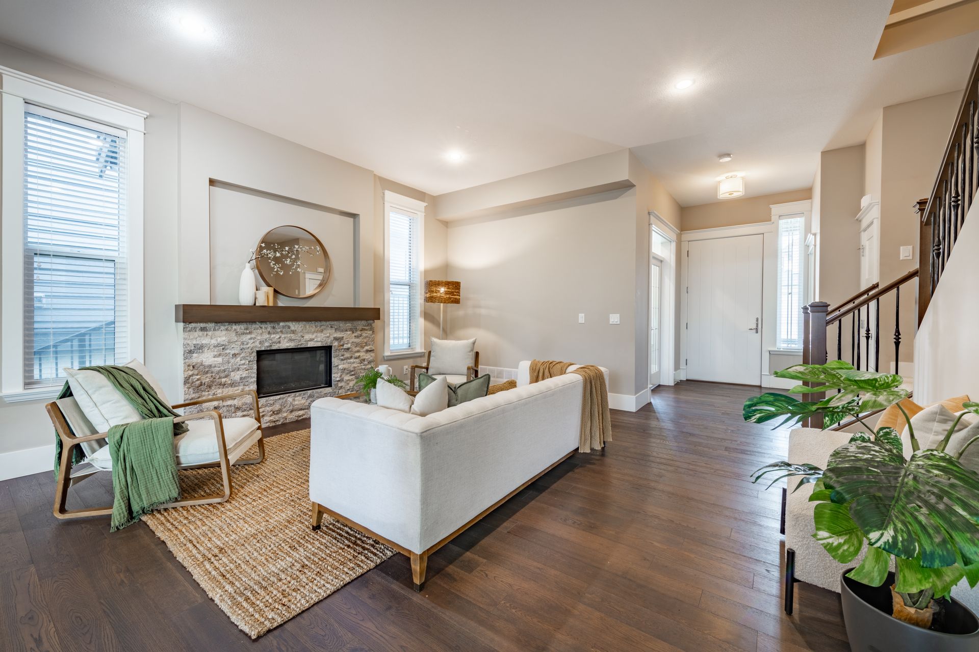 Bright living room with white sofa, fireplace, wicker chairs, dark wood floors, and hallway beyond