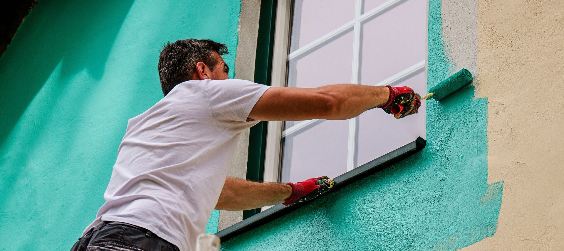 Person painting a turquoise wall with a roller on a ladder