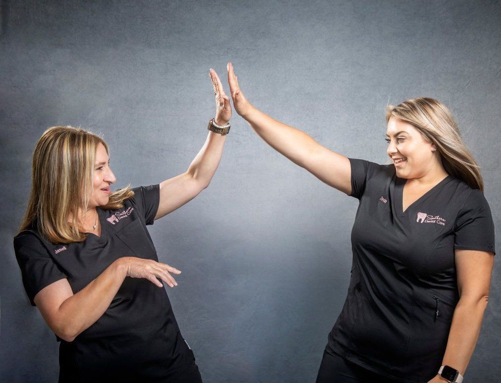 Two women in black scrubs are giving each other a high five.